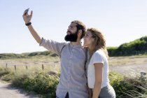 Casal jovem levando selfie smartphone no campo ensolarado — Fotografia de Stock