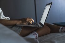 Gros plan de la femme assise sur le lit et utilisant un ordinateur portable — Photo de stock