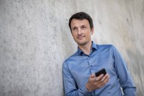 Portrait d'homme d'affaires souriant avec téléphone portable appuyé contre un mur en béton — Photo de stock