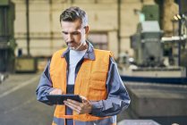 Man in protective workwear using tablet in factory — Stock Photo