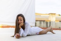 Porträt einer lächelnden jungen Frau, die auf der Dachterrasse liegt und ihr Handy benutzt — Stockfoto