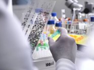 Científico sosteniendo un gel de ADN que revela la composición genética de la muestra en el vial - foto de stock