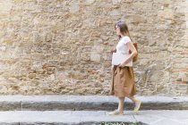 Donna che cammina lungo un muro di pietra che trasporta laptop — Foto stock