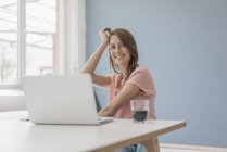Усміхнена жінка вдома сидить за столом з ноутбуком — стокове фото