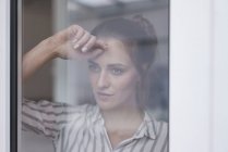 Крупним планом самотня жінка, що дивиться з вікна — стокове фото