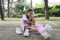 Menina sorrindo para a câmera enquanto coloca patins no parque — Fotografia de Stock