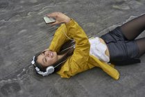Femme souriante avec écouteurs couchés sur le sol prenant selfie avec smartphone — Photo de stock