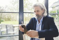 Homme d'affaires senior assis sur une chaise, en utilisant un smartphone — Photo de stock