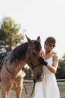 Portrait of woman in dress and helmet stroking horse outdoors — Stock Photo