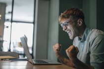 Jeune homme utilisant un ordinateur portable, riant avec succès — Photo de stock