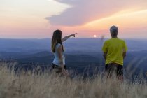 Senior father and adult daughter looking at view from top of hill during sunset — Stock Photo