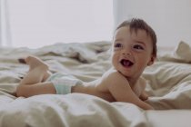 Bambino felice, sdraiato sul letto, ridendo — Foto stock
