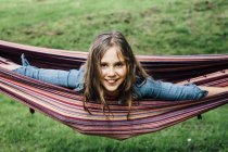 Portrait of smiling girl lying in hammock sticking out tongue — Stock Photo