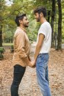 Glückliches junges schwules Paar hält Händchen im herbstlichen Park — Stockfoto