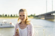 Retrato de una mujer sonriente comiendo helado en verano a orillas del río - foto de stock