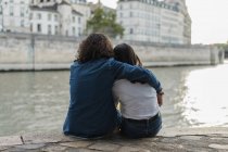 Francia, París, vista trasera de una joven pareja sentada en una pared en el río Sena - foto de stock