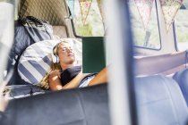 Woman with headphones lying in a van reading book — Stock Photo