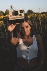 Mujer joven en un campo de girasoles sosteniendo una cámara instantánea - foto de stock