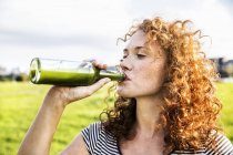 Retrato de ruiva jovem bebendo bebida de garrafa ao ar livre — Fotografia de Stock