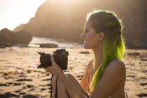 EE.UU., California, Costa Oeste, mujer joven con el pelo verde teñido y la cámara sentado en la playa - foto de stock