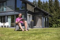 Sorridente uomo maturo seduto nel giardino della sua casa utilizzando un tablet — Foto stock
