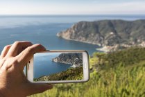 Italia, Liguria, Cinque Terre, imagen recortada del hombre tomando fotos de la bahía de Monterosso - foto de stock
