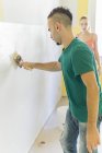 Uomo pittura muro a nuova casa mentre la ragazza lo guarda — Foto stock