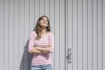 Mujer joven parada frente a la puerta del garaje y disfrutando del sol - foto de stock