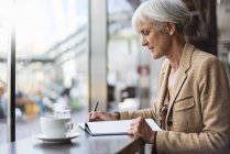 Senior businesswoman taking notes in cafe — Stock Photo