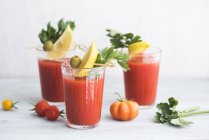 Glasses of fresh spicy tomato juice with cellery garnished with lemon slice, green olive and parsley — Stock Photo
