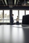 Empresário e empresária em pé na janela e laptop na mesa — Fotografia de Stock