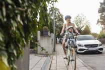 Мати і дочка їзда на велосипеді, дочка носіння шолом і сидячи в дитячому кріслі — стокове фото
