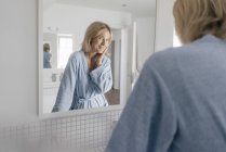 Portrait de femme mature souriante regardant miroir de salle de bains — Photo de stock