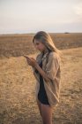 Молодая женщина, стоящая в поле, используя смартфон — стоковое фото