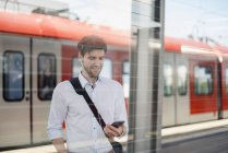 Улыбающийся бизнесмен на платформе станции с наушниками и сотовым телефоном — стоковое фото