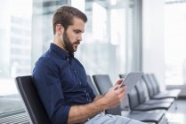 Young businessman sitting in waiting area using tablet — Stock Photo