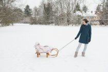 Mother pulling little daughter on sledge — Stock Photo