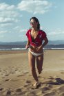 Portrait of laughing teenage girl in sunglasses running on beach — Stock Photo