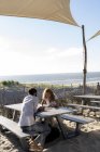 Coppia giovane con tablet digitale, seduta a tavola sulla spiaggia — Foto stock