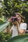Giovane donna in serra, scattare foto con fotocamera istantanea — Foto stock