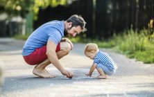 Father and his little daughter drawing with chalks on street in summer — Stock Photo