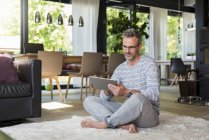 Mature homme assis sur le tapis à la maison à l'aide d'une tablette — Photo de stock