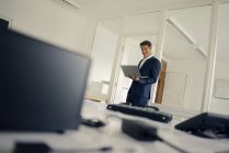 Empresário de pé no escritório, usando laptop — Fotografia de Stock