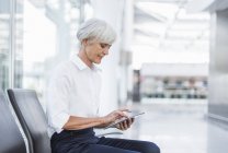 Senior businesswoman sitting in waiting area and using tablet — Stock Photo