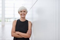 Portrait of smiling senior woman wearing black dress leaning against wall — Stock Photo
