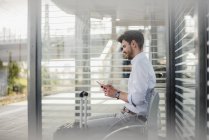 Geschäftsmann sitzt mit Handy auf Bahnsteig — Stockfoto