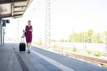Mulher de negócios madura com smartphone e mala andando na plataforma — Fotografia de Stock