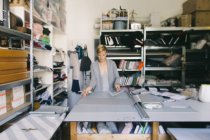 Femme blonde styliste en studio travaillant avec tissu gris textile à table — Photo de stock