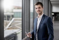 Retrato de jovem empresário sorridente em uma passagem com celular e fones de ouvido — Fotografia de Stock