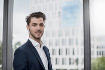 Porträt eines selbstbewussten jungen Geschäftsmannes mit Ohrhörern am Fenster — Stockfoto